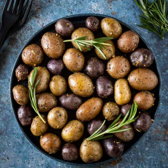 Overhead shot of roasted potatoes garnished with fresh rosemary on a black plate.