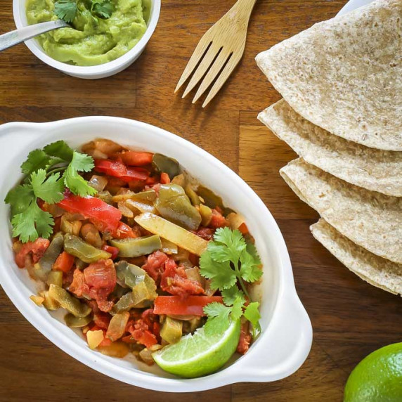 Overhead shot of veggie fajitas in a white dish garnished with cilantro with tortillas on the side.