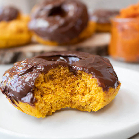 pumpkin spice donut with chocolate frosting with a bite taken on a white plate