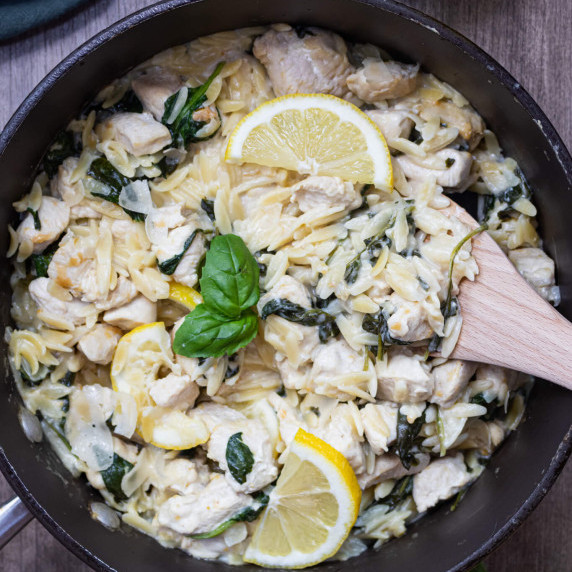 bowl of chicken and orzo dinner recipe with a wooden spoon
