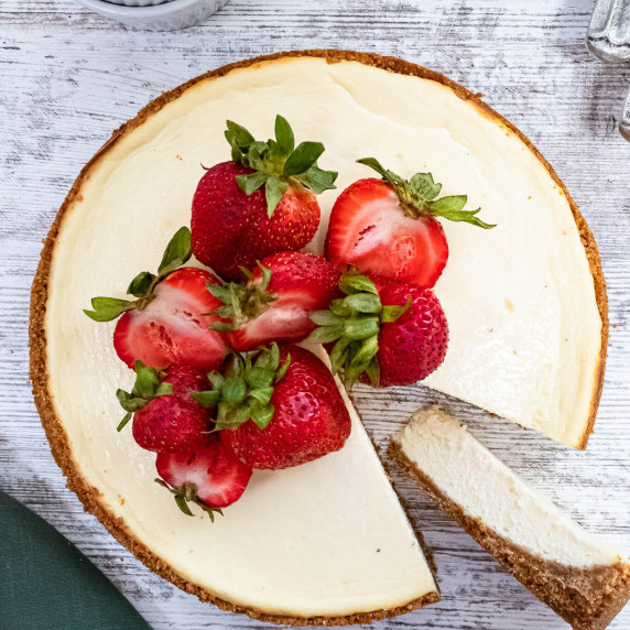 Classic cheesecake with strawberries on top on a white wood surface