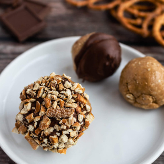 Peanut butter protein ball covered in chocolate and pretzels on a white plate