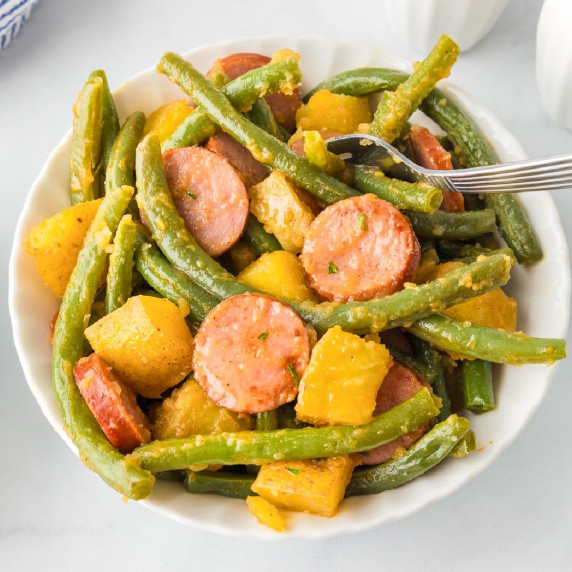 A bowl on a dinner table of green beans, sliced sausage, and chunks of potatoes. 