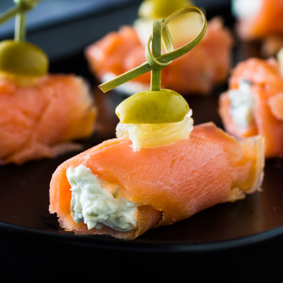 Side view of multiple smoked salmon bites on a black plate.