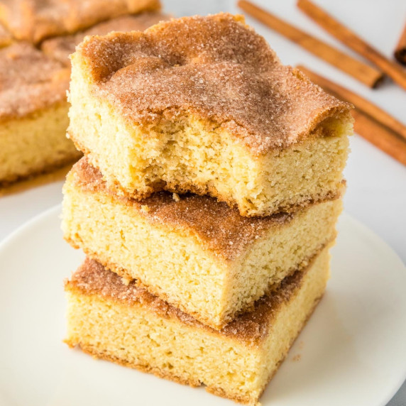 3 squares of snickerdoodle cookie bars stacked high on a plate.  The top cookie bar missing a bite.