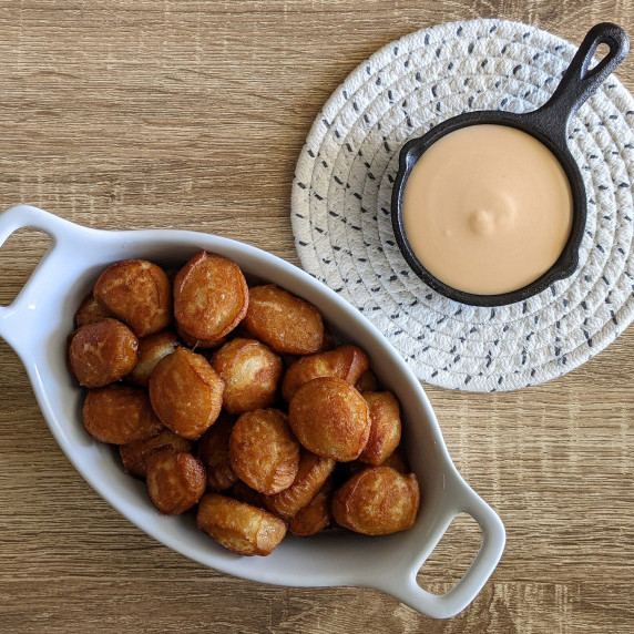 A serving dish of soft pretzel bites with a cast iron skillet of beer cheese dip
