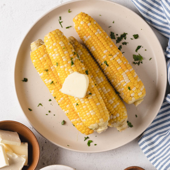 four ears of corn on a white plate covered in butter and cilantro. 