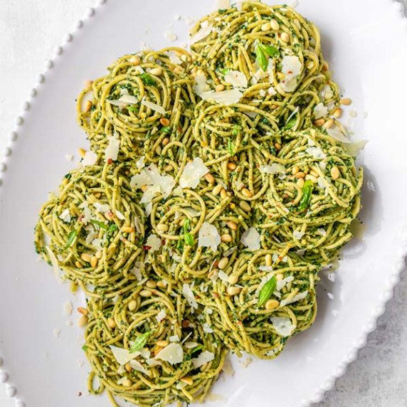 Spaghetti covered in pesto sauce on a white oval sharing platter.