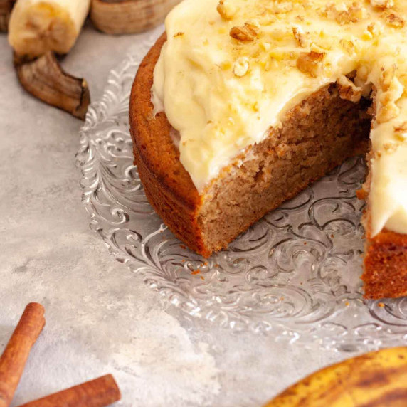 A cut spiced banana cake next to ripe bananas and cinnamon sticks.