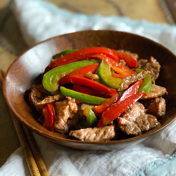 Stir fried beef with red and green bell peppers in a brown bowl.