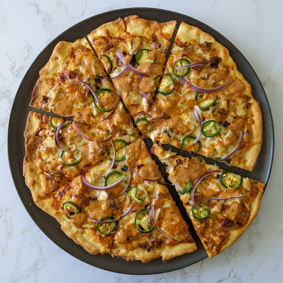 A homemade spicy chicken bacon ranch pizza topped with red onion and jalapeno slices