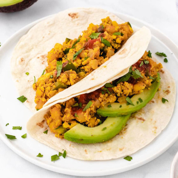 Spicy tofu scramble tacos with avocado slices on a white plate.