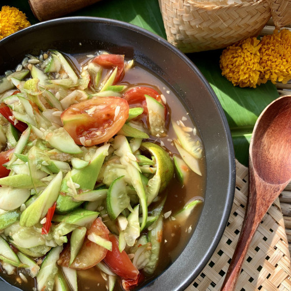 Top-view of spicy Lao cucumber salad with tomatoes in a black dish.