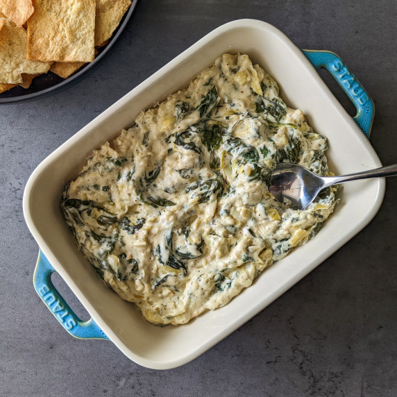 A serving dish of cheesy spinach and artichoke dip served with pita chips