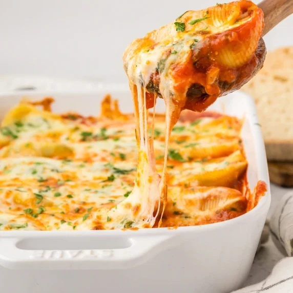 Spinach Stuffed Shells scooped out of dish with a wooden spoon.