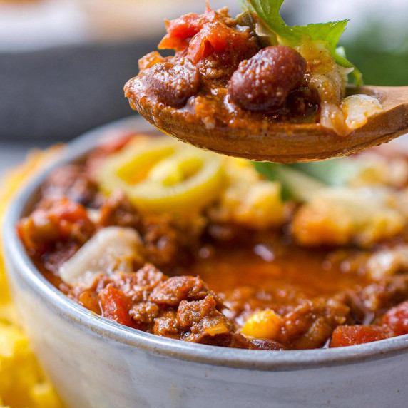 A spoonful of chili hovering above a bowl filled with chorizo chili.