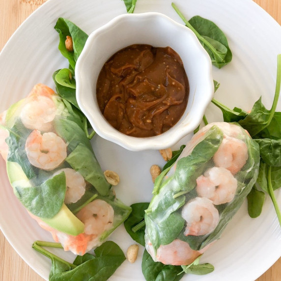 Freshly made spring rolls served on a white plate with hoisin peanut sauce for dipping