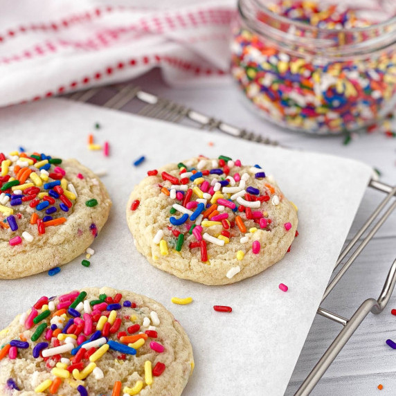 Sprinkle Cookies on a cooling rack with a jar of rainbow sprinkles nearby.