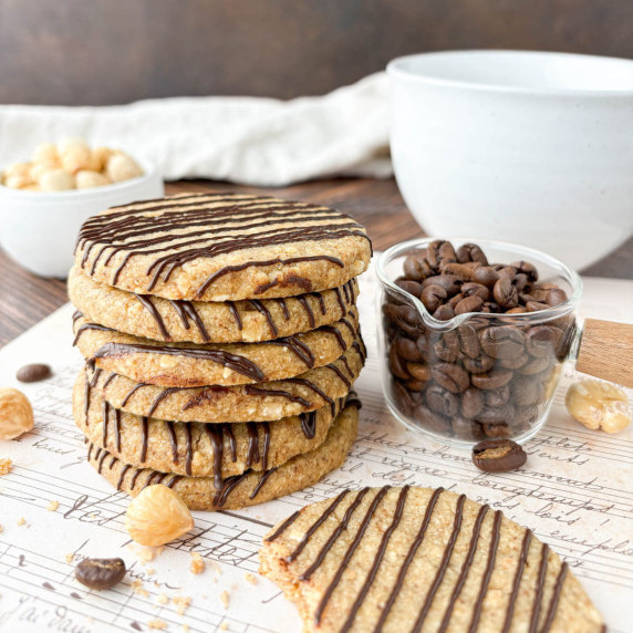 Six Hazelnut Espresso Shortbread Cookies stacked on sheet music with hazelnuts nearby.