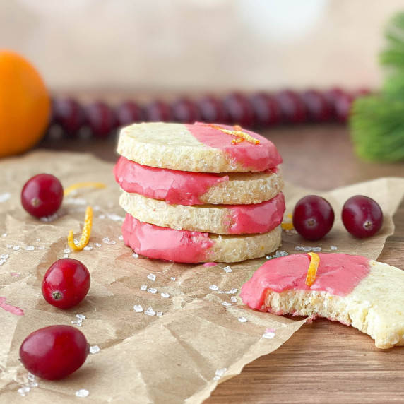 Stack of orange shortbread cookies with cranberry glaze on parchment paper with fresh cranberries.