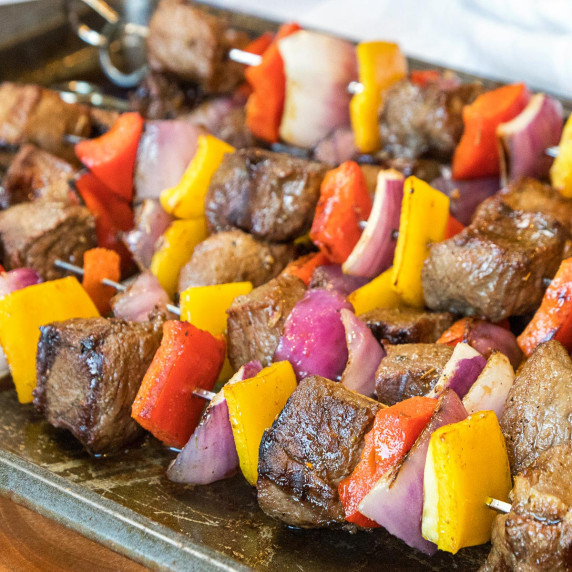 Steak, peppers, and onions on a skewer covered in marinade for the grill.