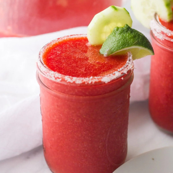 A mason jar drinking glass is rimmed with salt and filled with frozen strawberry cucumber margarita.