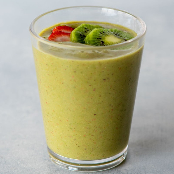 A green smoothie in a tall glass topped with thin slices of kiwi and strawberry as garnish.