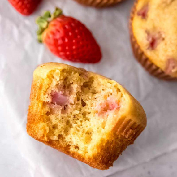 A strawberry muffin lying on its side with a bite taken out of it showing pockets of pink fruit.