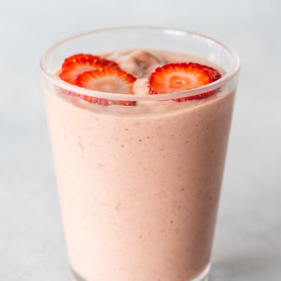 A pink strawberry shortcake smoothie topped with thin slices of fresh strawberry in a tall glass.