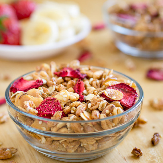 Side view of granola and strawberries in a clear bowl on a wooden surface.