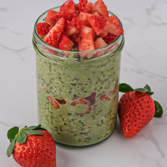 Mason jar with matcha overnight oats and two strawberries next to the jar 