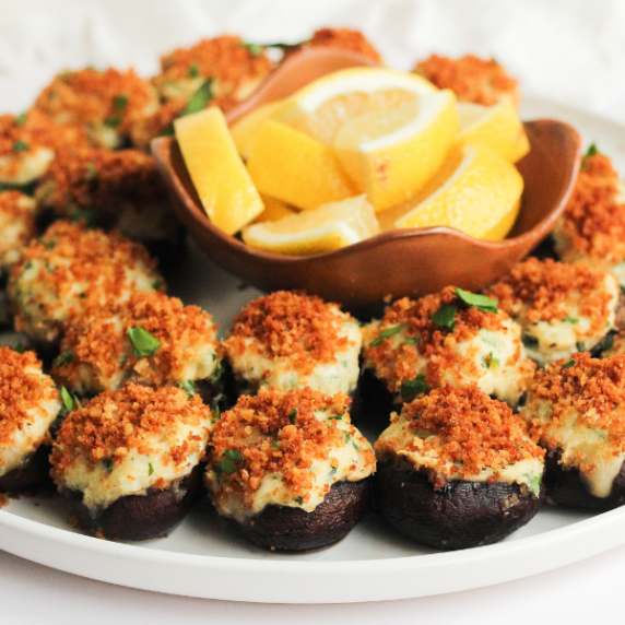 Stuffed mushrooms with crab on a white plate, and a brown bowl with lemon wedges.