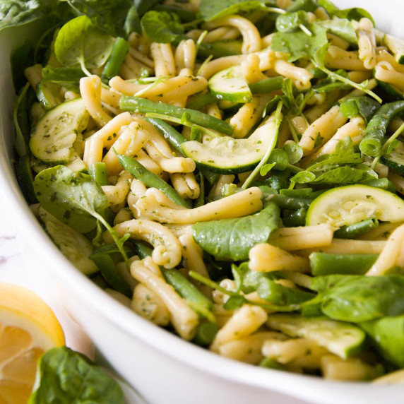Green vegetable pasta salad in a white bowl next to a halved lemon.