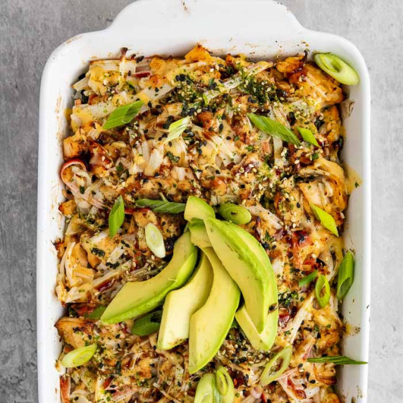 Overhead shot of sushi bake garnished with sliced green onions and avocado in a casserole dish.