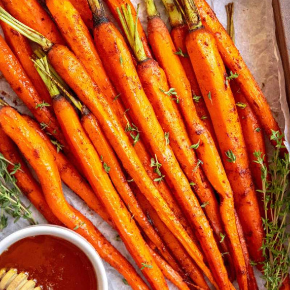 Honey glazed whole carrots on a parchment lined serving tray with fresh thyme and additional honey.