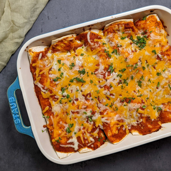 A casserole dish of enchiladas topped with shredded cheese