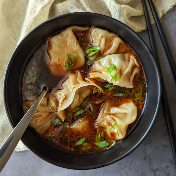 A bowl of spicy Szechuan soup with homemade pork dumplings