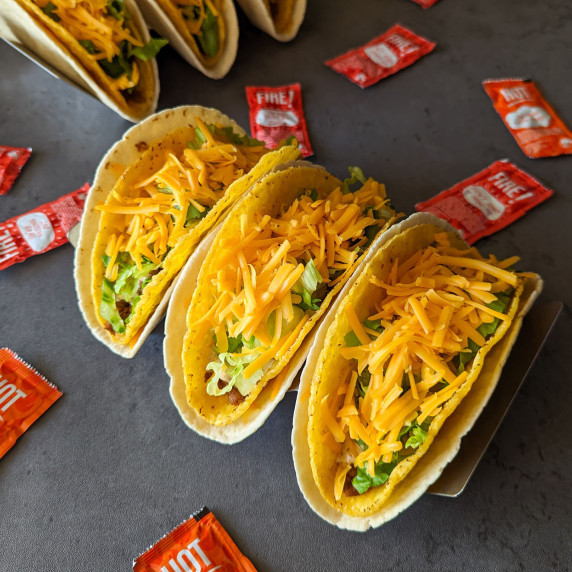 Three Taco Bell cheesy gordita crunch tacos with hot sauce