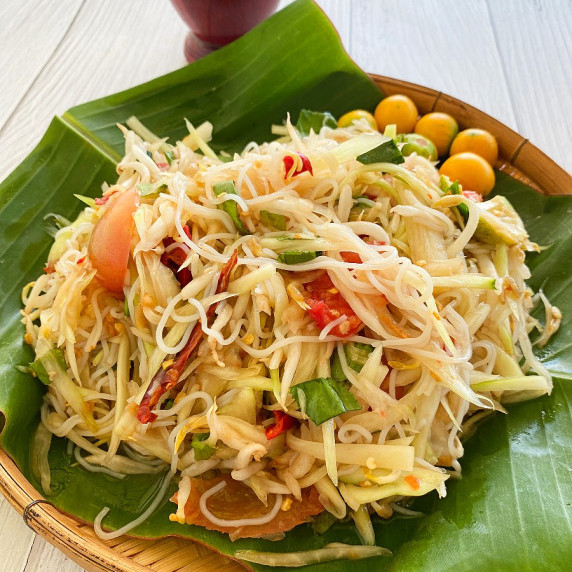 Tam sua with tomatoes on a banana leaf in a bamboo serving dish on a white background.