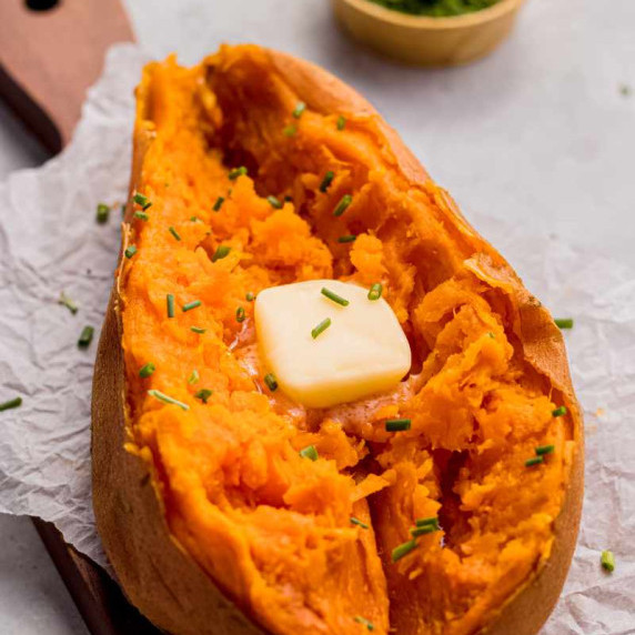 Close view of a tender sweet potato split down the center with a pat of butter and snipped chives.