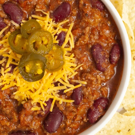 Copycat Texas Roadhouse chili with kidney beans, topped with cheese and jalapeños in a white bowl