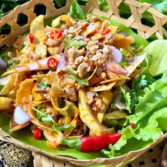 Thai banana blossom salad served in a bamboo dish on a bed of lettuce.