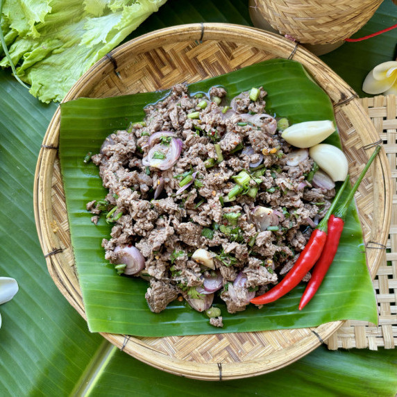 Top-view of Thai beef larb served with chilies and garlic in a bamboo woven dish.