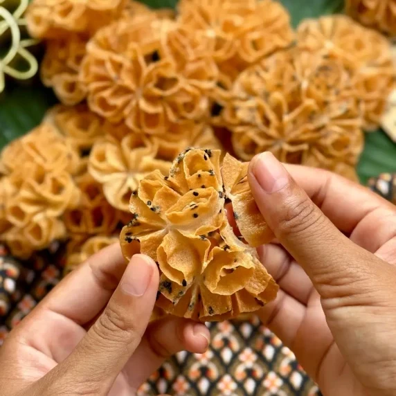 Close-up of a hand holding a freshly made Thai lotus flower cookie.