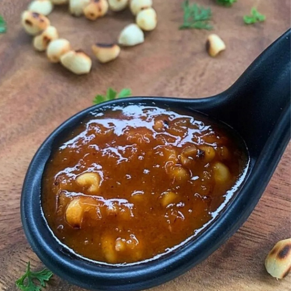 Authentic Thai peanut sauce in a black sauce spoon with peanuts in heart shape above it.