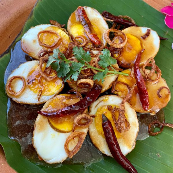 Boiled Thai son-in-law eggs on a banana leaf, topped with dried chilies, fried shallots, and sauce.