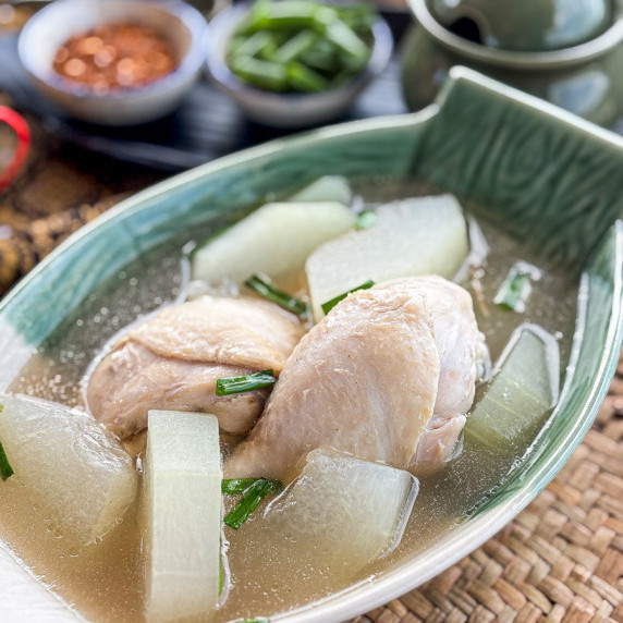 Thai winter melon soup with chicken drumsticks served in a green dish.
