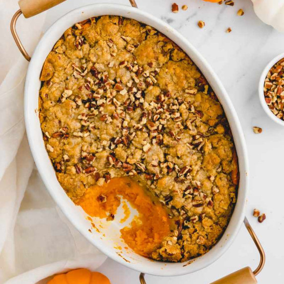 Overhead of a sweet potato casserole in a white baking dish with a scoop taken out.
