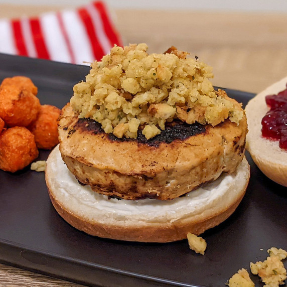 A turkey burger on a potato bun topped with leftover stuffing and cranberry sauce from Thanksgiving