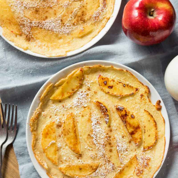 Two thin dutch pancakes with sliced apples baked in and topped with powdered sugar on white plates.